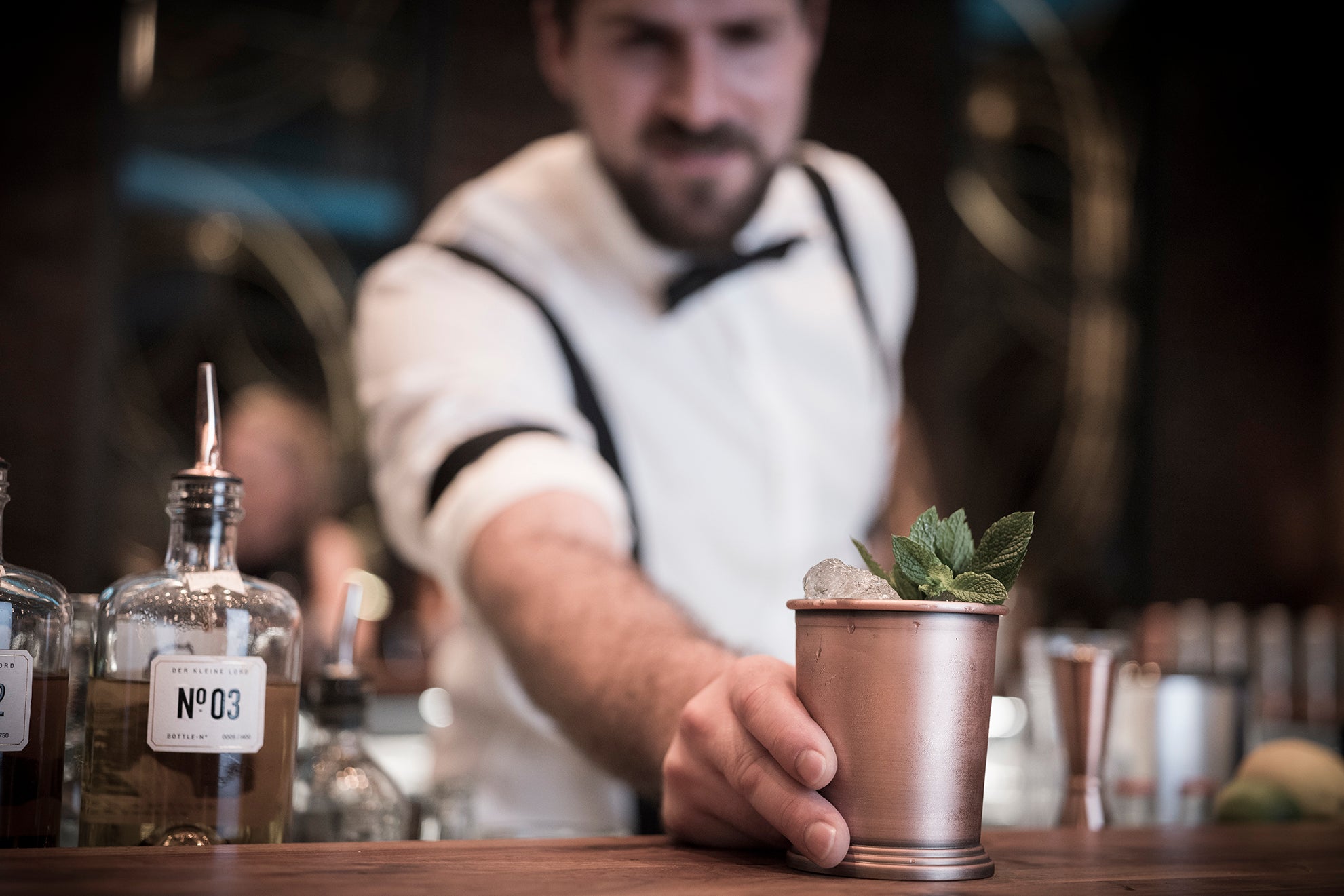 Buddy schiebt einen fertigen Cocktail an der Bar nach vorne. In dem antiken Edelstahl Becher ist Eis und Minze