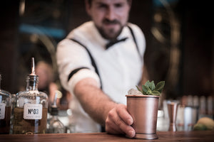 Buddy schiebt einen fertigen Cocktail an der Bar nach vorne. In dem antiken Edelstahl Becher ist Eis und Minze