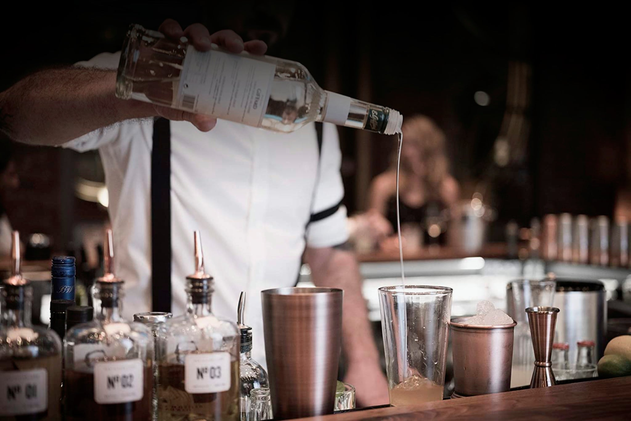 Buddy steht in der Bar und schüttet Alkohol in ein Glas. Danaben sind Shaker und andere Getränke.